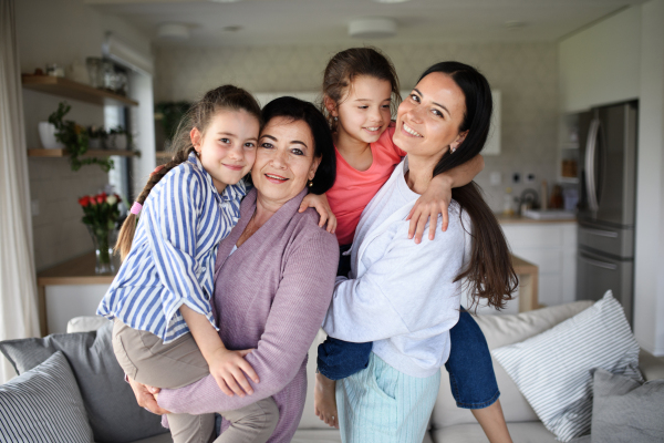 Portrait of happy small girls with mother and grandmother indoors at home, looking at camera.