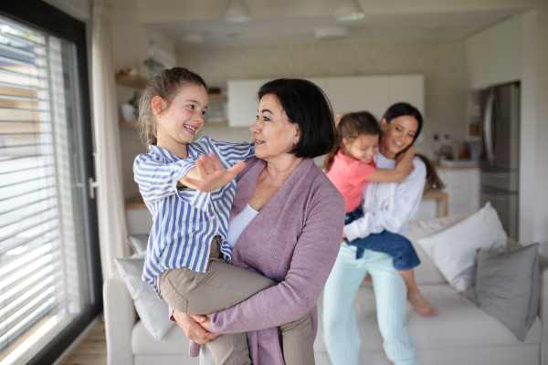 Happy small girls with a mother and grandmother indoors at home, having fun.