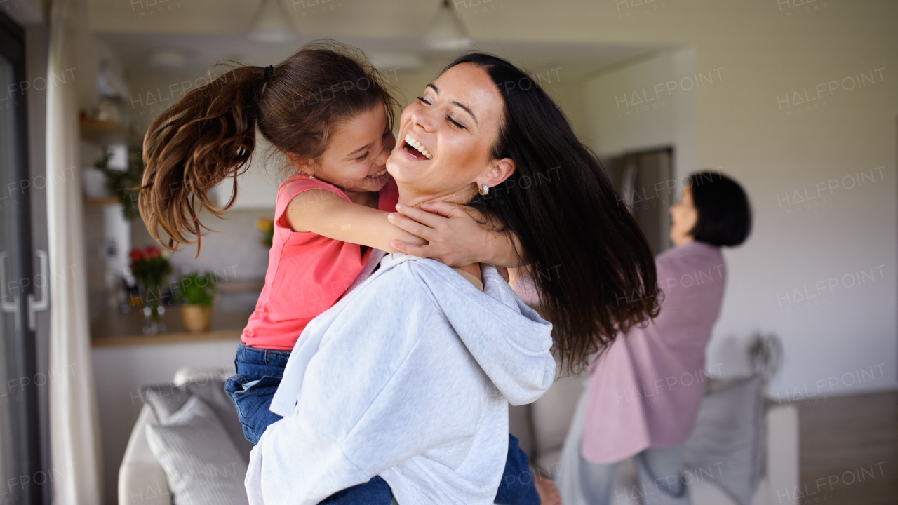 A happy small girl with mother indoors at home, having fun, hugging.