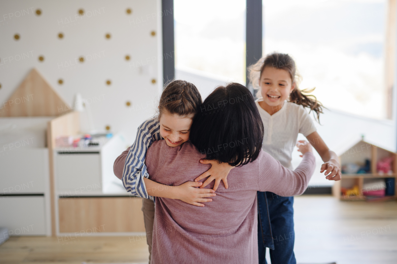 Happy small girls greeting a senior grandmother indoors at home, hugging.