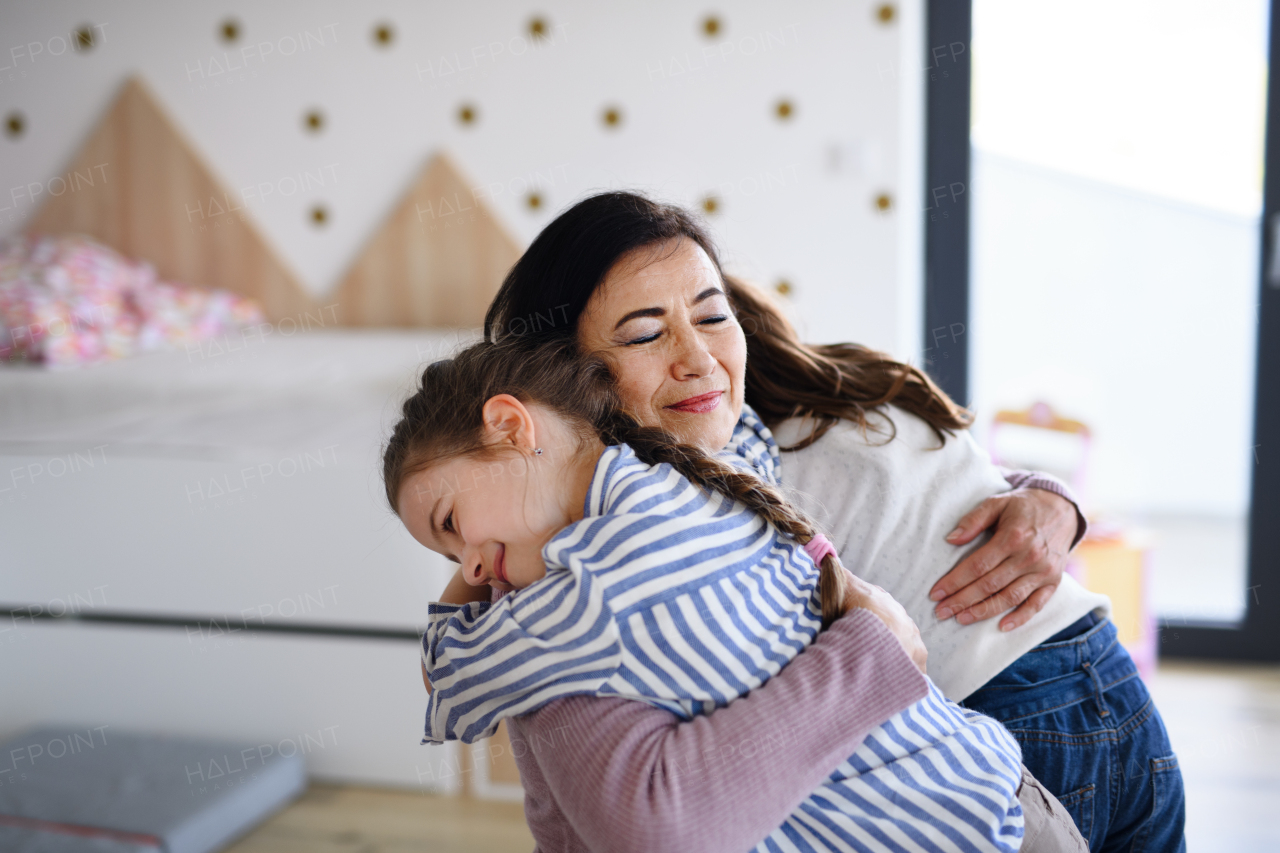 Happy small girls greeting a senior grandmother indoors at home, hugging.