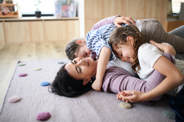 Happy small girls with senior grandmother indoors at home, playing on floor in bedroom.