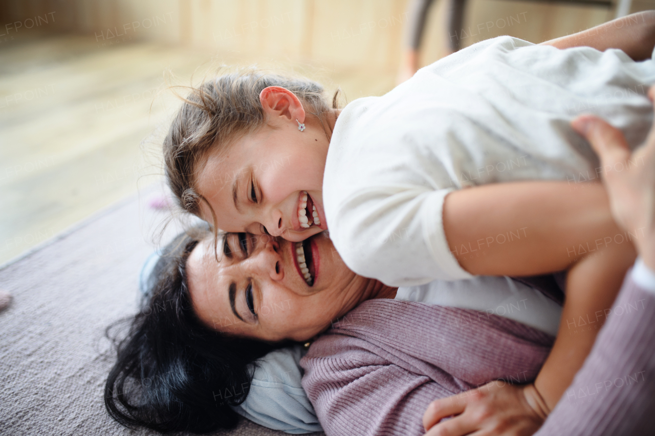 A happy small girl with senior grandmother indoors at home, playing on floor.