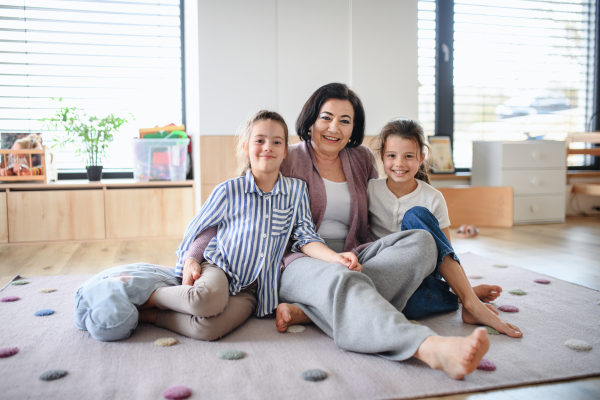 Happy small girls with senior grandmother indoors at home, playing on floor in bedroom.