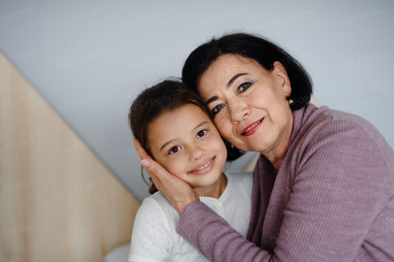 A happy small girl with senior grandmother indoors at home looking at camera.