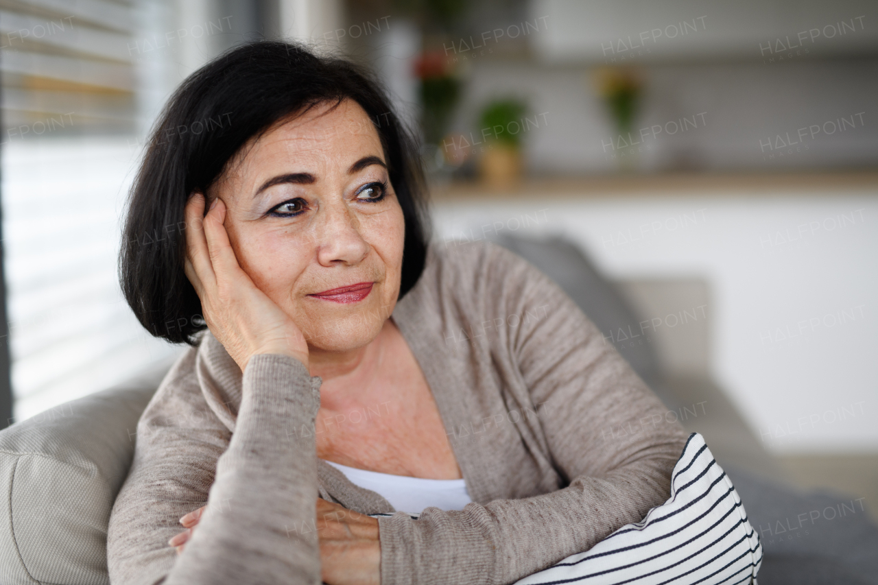 A close up of happy senior woman sitting on sofa and looking away indoors at home.