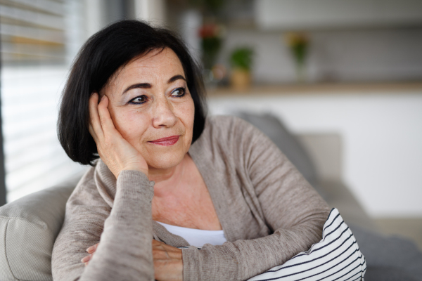 A close up of happy senior woman sitting on sofa and looking away indoors at home.