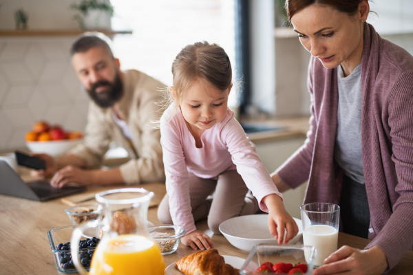 A family with small daughter indoors in kitchen, everyday life and home office with child concept.