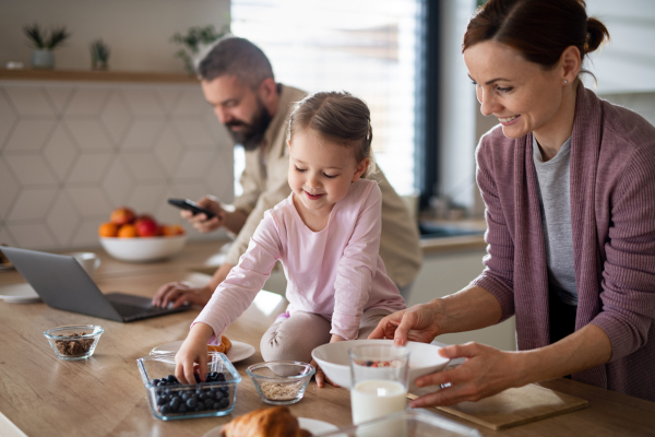 A family with small daughter indoors in kitchen, everyday life and home office with child concept.