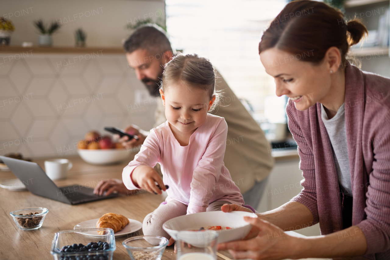 A family with small daughter indoors in kitchen, everyday life and home office with child concept.