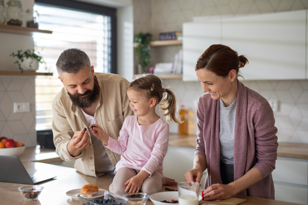 A family with small daughter indoors in kitchen, everyday life and home office with child concept.