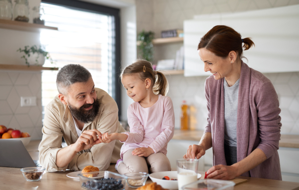 A family with small daughter indoors in kitchen, everyday life and home office with child concept.