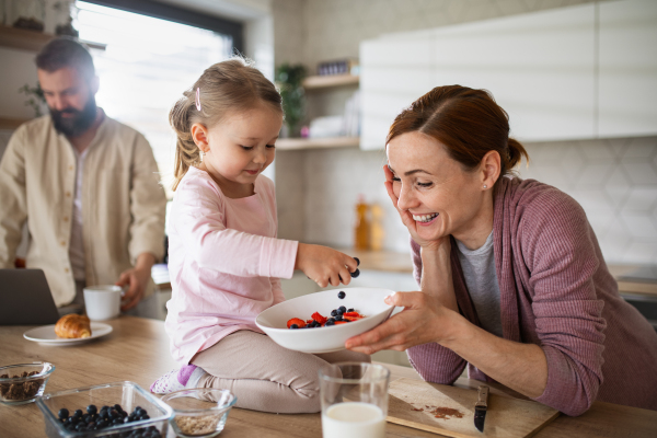 A family with small daughter indoors in kitchen, everyday life and home office with child concept.