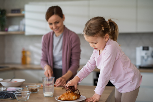 Happy mother with small daughter indoors in kitchen at home preparing breakfast, everyday life concept.