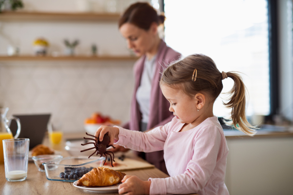 Happy mother with small daughter indoors in kitchen at home preparing breakfast, everyday life concept.