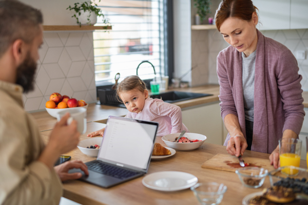 A family with small daughter indoors in kitchen, everyday life and home office with child concept.