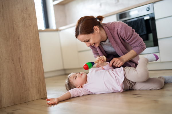 A happy mother with small daughter playing indoors in kitchen, laughing.