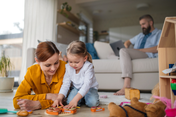 A mother with small daughter playing indoors at home, everyday life and home office with child concept.