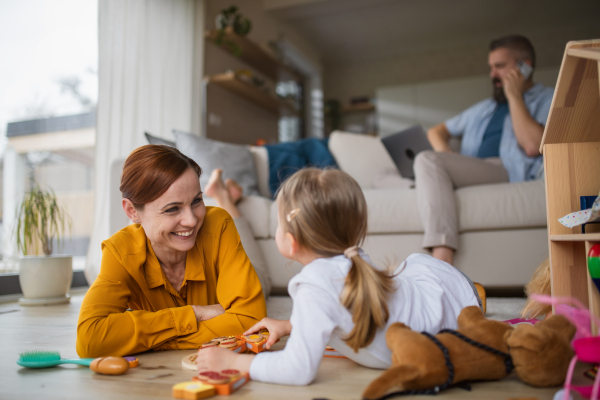 A mother with small daughter playing indoors at home, everyday life and home office with child concept.