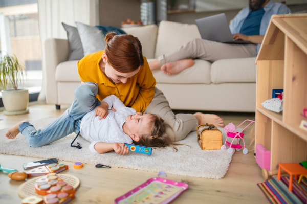 A mother with small daughter playing indoors at home, everyday life and home office with child concept.