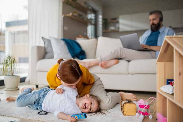 A mother with small daughter playing indoors at home, everyday life and home office with child concept.