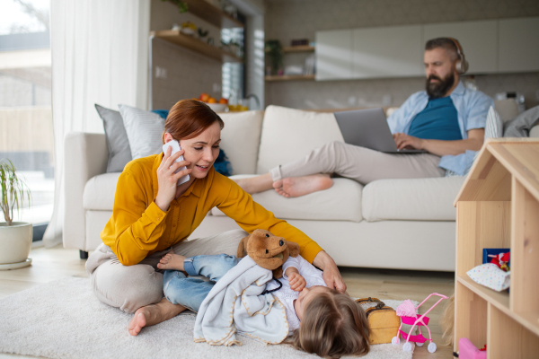 A mother with small daughter playing and working indoors at home, everyday life and home office with child concept.