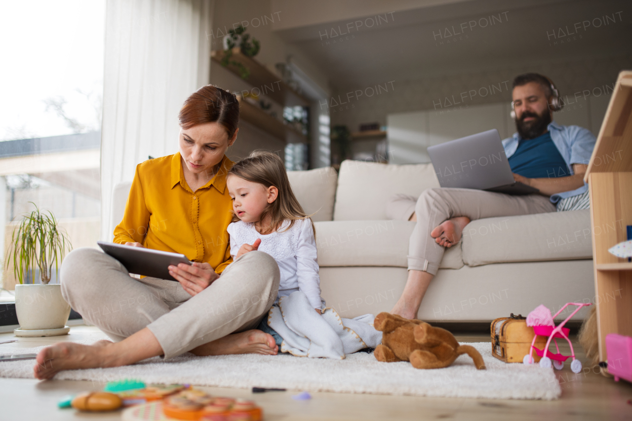 A mother with small daughter using tablet indoors at home, everyday life and home office with child concept.