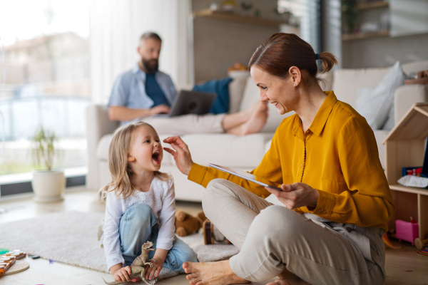 A mother with small daughter playing and working indoors at home, everyday life and home office with child concept.