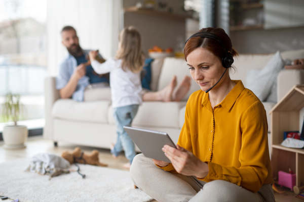 Businesswoman with tablet and headset working indoors at home, everyday life and home office with child concept.