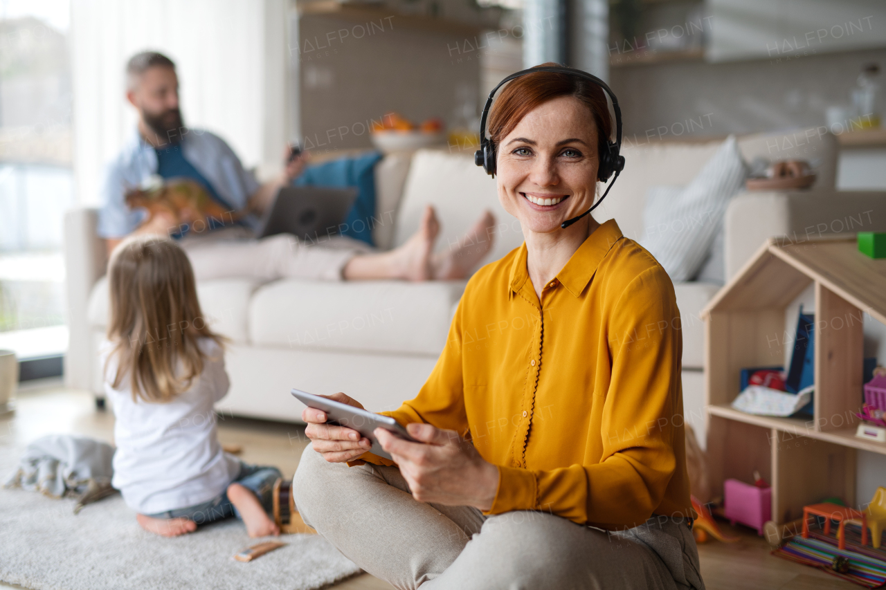 Businesswoman with tablet and headset working indoors at home, everyday life and home office with child concept.