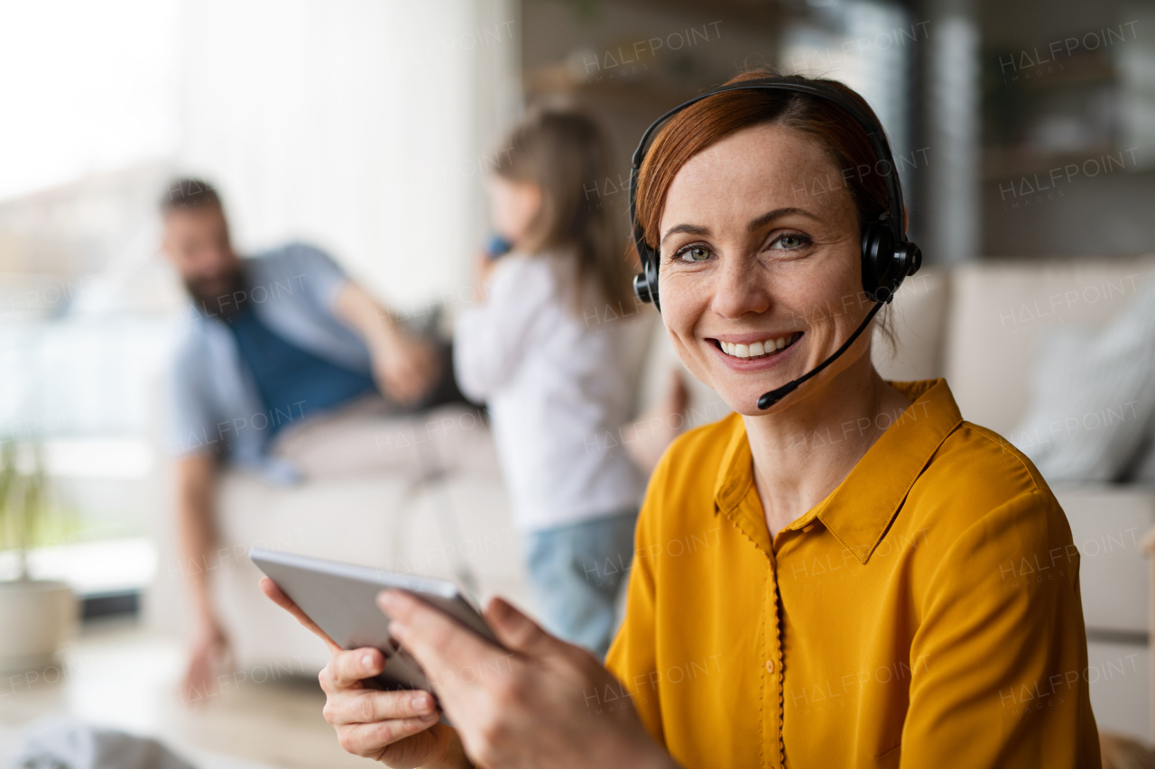 Businesswoman with tablet and headset working indoors at home, everyday life and home office with child concept.