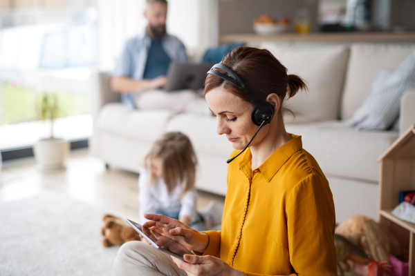 Businesswoman with tablet and headset working indoors at home, everyday life and home office with child concept.