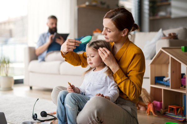 A mother beushing hair to her small daugter indoors at home, everyday life and home office with child concept.