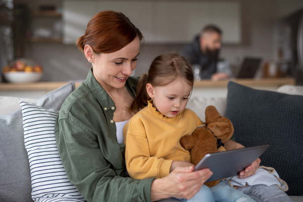 A happy mother with small daughter watching kids programme on tablet indoors at home, single parenting concept.