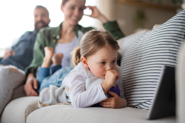 A family with small daughter watching programme on tablet indoors at home, everyday life concept.