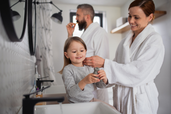 A father and mother with small daughter washing indoors in bathroom in the evening or morning.