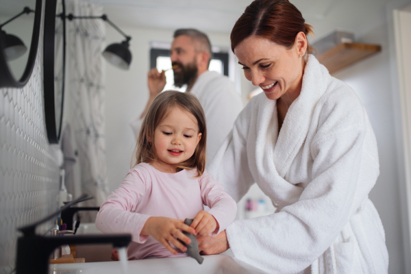 A father and mother with small daughter washing indoors in bathroom in the evening or morning.