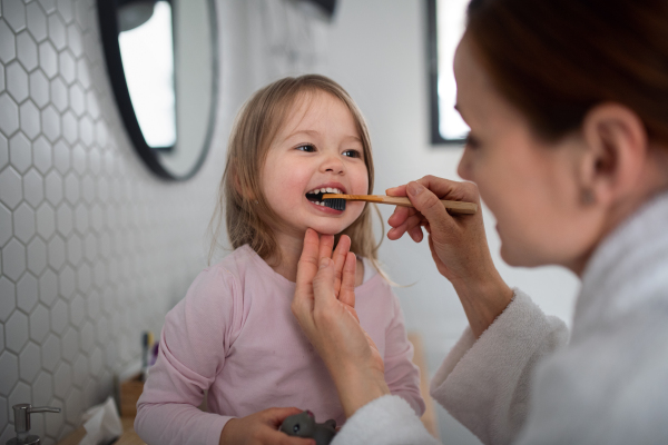 Mother with happy small daughter brushing teeth indoors in bathroom in the evening or morning.