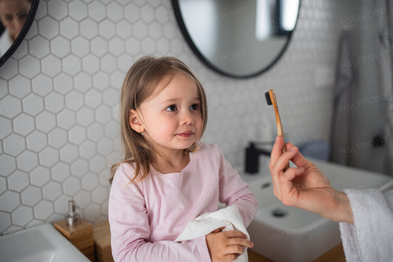 Unrecognizable mother with a small daughter brushing teeth indoors in bathroom in the evening or morning.