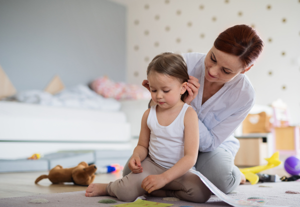 A happy mother with small daughter playing indoors in bedroom, laughing.