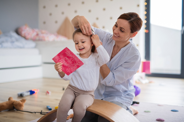 A happy mother with small daughter playing indoors in bedroom, laughing.