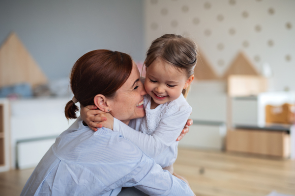 A happy mother with small daughter hugging indoors in bedroom, laughing.