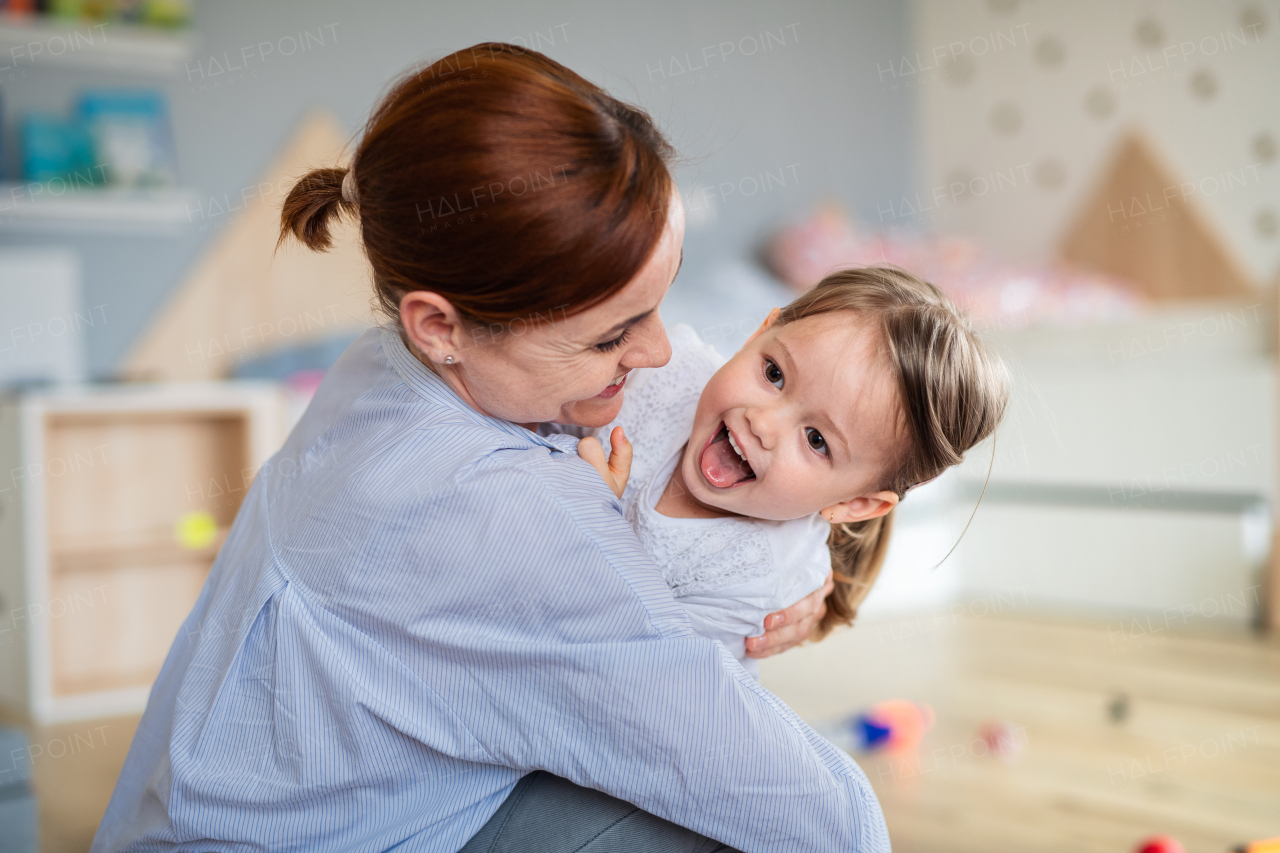 A happy mother with small daughter playing indoors in bedroom, laughing.