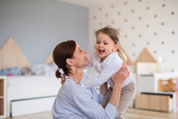 A happy mother with small daughter playing indoors in bedroom, laughing.