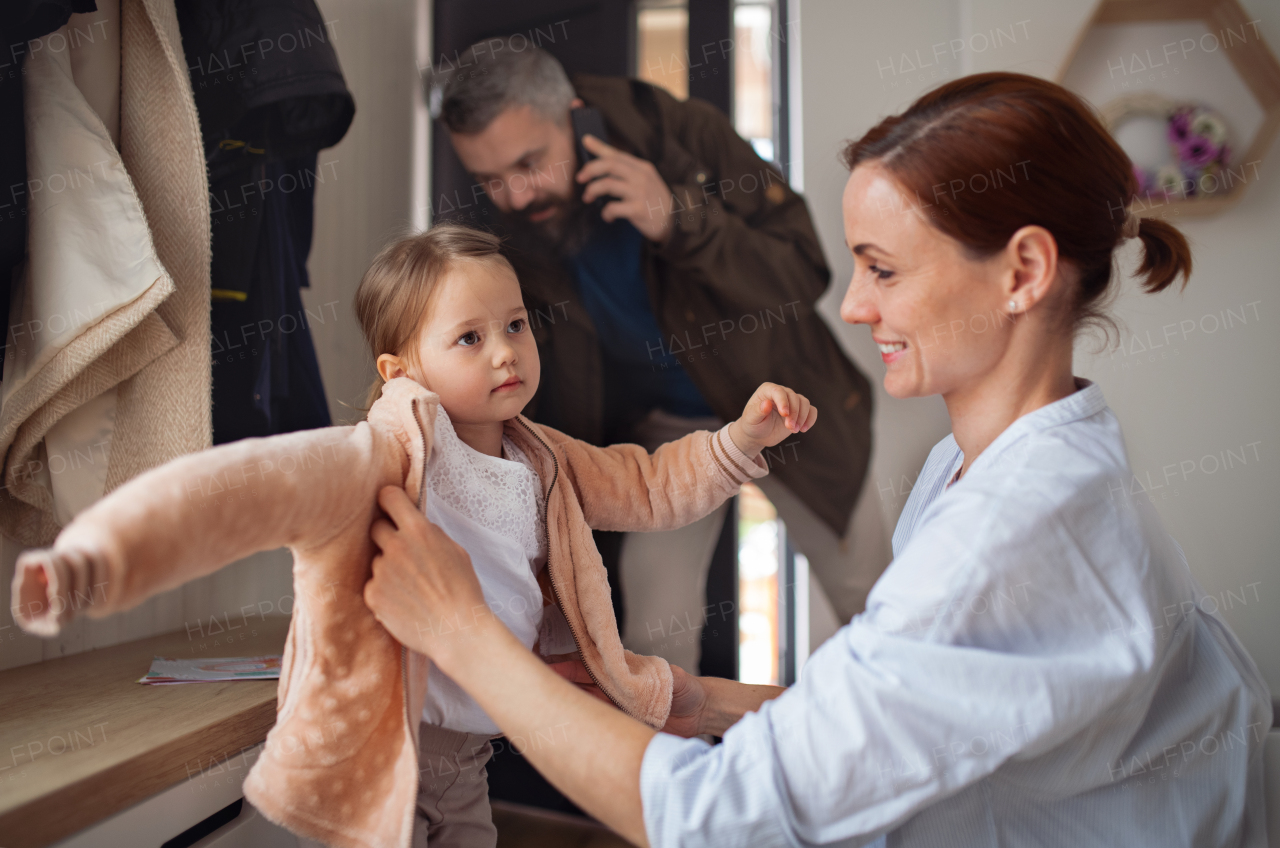 Busy father and mother with small daughter in entrance hall indoors in the morning, leaving for work and nursery school.