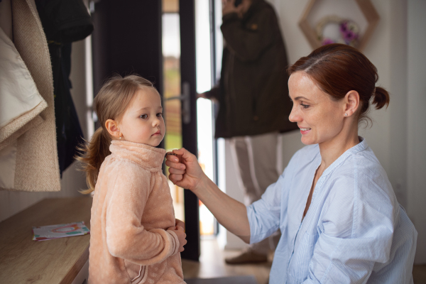 Mother with a small daughter in entrance hall indoors in the morning, leaving for work and nursery school.