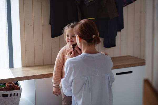 Mother with a small daughter in entrance hall indoors in the morning, leaving for work and nursery school.