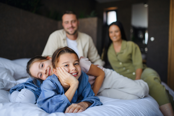 A happy young family with two children lying on bed at hotel, summer holiday.