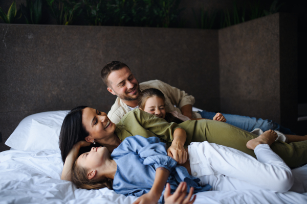 A happy young family with two children lying on bed at hotel, summer holiday.