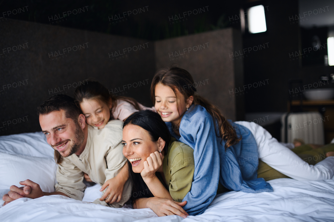 A happy young family with two children lying on bed at hotel, summer holiday.